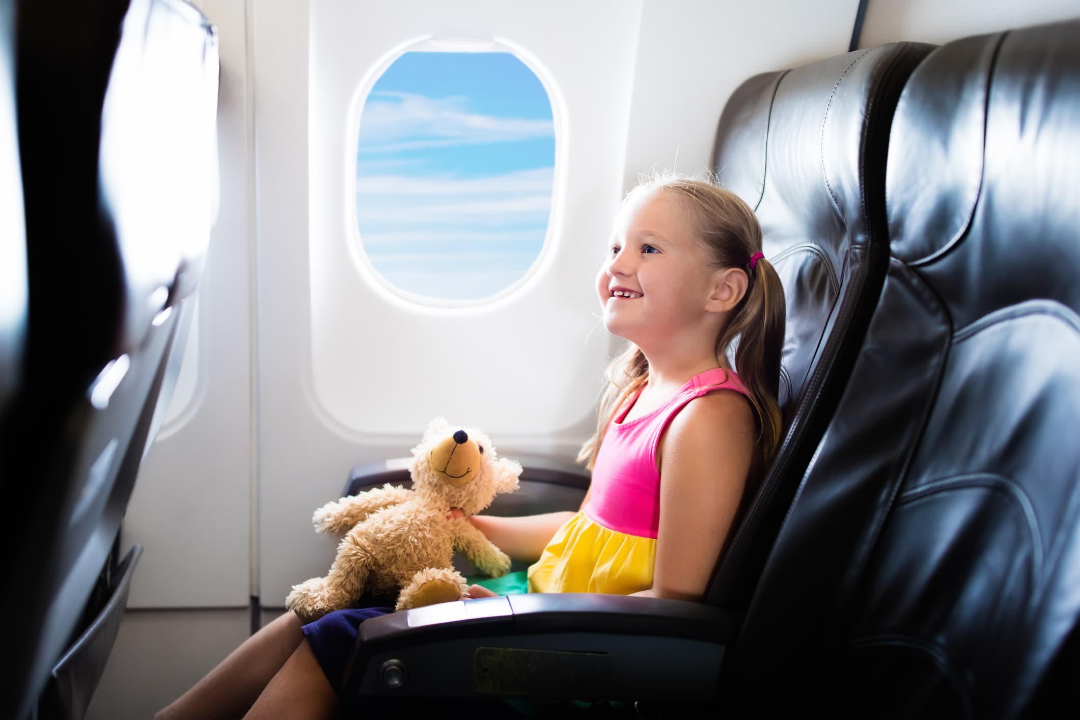 Little girl holding a teddy bear in an airplane window seat